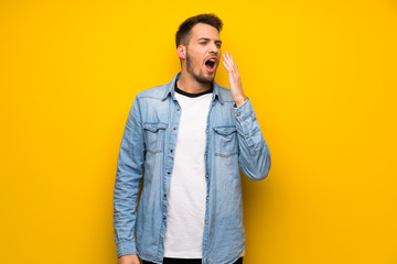 Handsome man over yellow wall yawning and covering wide open mouth with hand