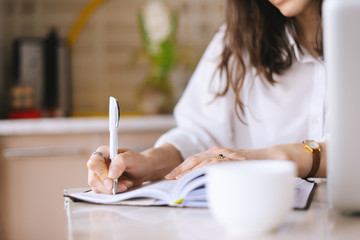 Close up of a woman writer hand writing in a notebook at home in the kitchen - Powered by Adobe