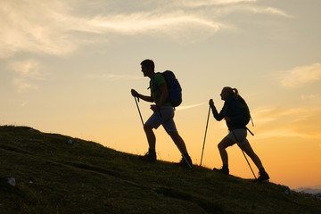SILHOUETTE Active man and his girlfriend trek up a mountain right before sunrise - obrazy, fototapety, plakaty