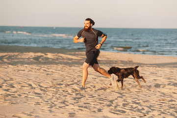 Running man. Male runner jogging with dog during the sunrise on beach