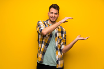 Handsome man over yellow wall holding copyspace to insert an ad