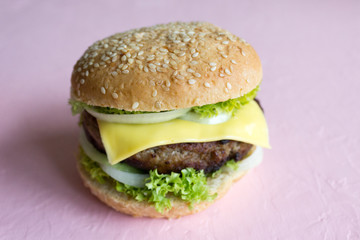 Delicious homemade burger with beef, cheese and salad on a pink background