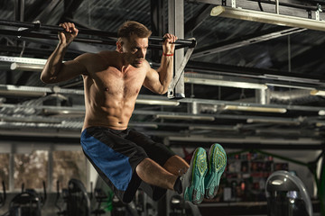 Hardcore sport. Handsome young focused male athlete with toned strong muscular body doing leg raise...