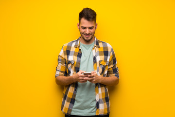 Handsome man over yellow wall sending a message with the mobile
