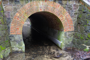 Stone culvert over the road for a small river. A small stream in a forest area.
