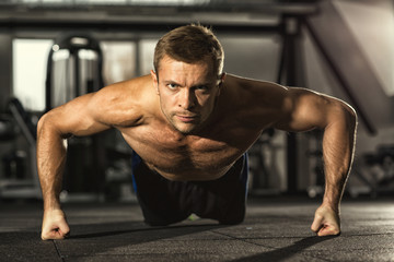 Obraz premium No way back. Handsome young serious motivated fitness man looking to the camera confidently doing pushups at the gym workout muscular power strength endurance energy sport health challenge concept