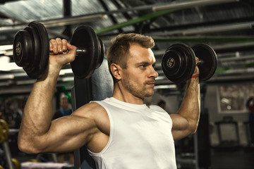 Fototapeta na wymiar Pump it up! Young handsome serious fitness man doing weight lifting exercises with dumbbells at the gym motivation challenge sports achievement goals lifestyle masculinity strength powerful concept