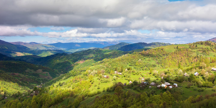 countryside of panorama in springtime. village on the hillside, mountain ridge in the distance. sunny weather with clouds on the sky. view from the hill. 