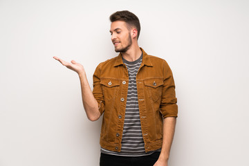 Handsome man over white wall holding copyspace imaginary on the palm to insert an ad