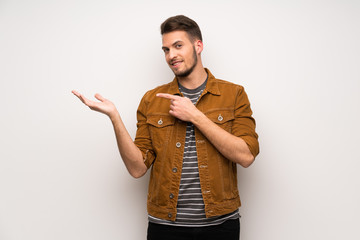 Handsome man over white wall holding copyspace imaginary on the palm to insert an ad