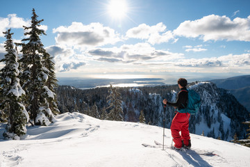 Adventurous man is backcountry skiing up Mount Seymour during a sunny winter day. Taken in North Vancouver, BC, Canada.