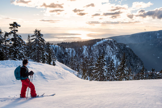Adventurous man is backcountry skiing up Mount Seymour during a sunny winter day. Taken in North Vancouver, BC, Canada.