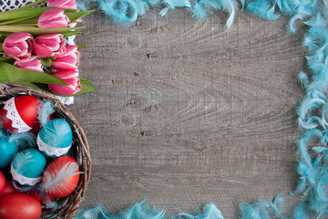 Wielkanocne tło z różowymi tulipanami, koszykiemi pełnym pisanek i niebieskimi piórami