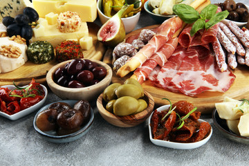Italian antipasti wine snacks set. Cheese variety, Mediterranean olives, crudo, Prosciutto di Parma, salami and wine in glasses over grunge background.