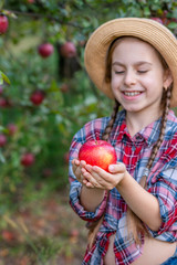 Portrait of a cute girl in a farm garden with a red apple.