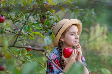 Portrait of a cute girl in a farm garden with a red apple.