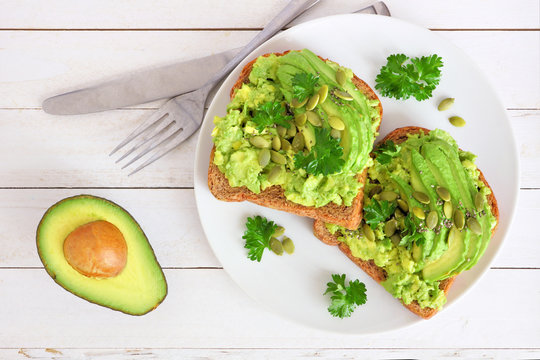 Avocado toasts with pumpkin and chia seeds on whole grain bread. Above view on a white wood background.
