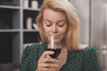 Gorgeous young woman smiling with her eyes closed, smelling delicious red wine in her glass....