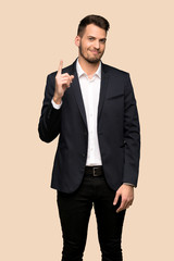 Handsome business man showing and lifting a finger in sign of the best over ocher background