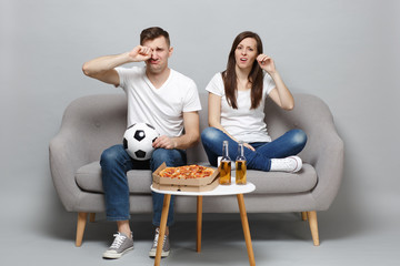 Upset crying couple woman man football fans cheer up support favorite team with soccer ball wiping tears isolated on grey background in studio. People emotions, sport family leisure lifestyle concept.