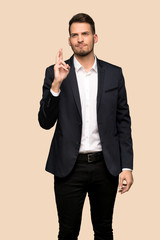 Handsome business man with fingers crossing and wishing the best over ocher background