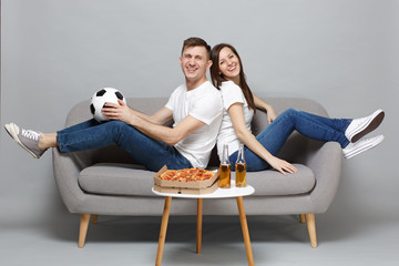 Smiling couple woman man football fans cheer up support favorite team with soccer ball, sitting back to back isolated on grey wall background. People emotions, sport family leisure lifestyle concept.