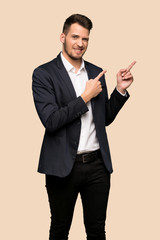 Handsome business man frightened and pointing to the side over ocher background