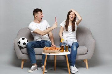 Irritated couple woman man football fans cheer up support favorite team swearing, holding megaphone, red card isolated on grey wall background. People emotions, sport family leisure lifestyle concept.