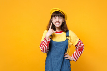 Cheerful girl teenager in french beret with closed eyes, horns up gesture, depicting heavy metal rock sign, rock-n-roll isolated on yellow wall background. People emotions concept. Mock up copy space.