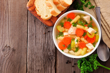 Homemade chicken noodle soup with vegetables. Top view table scene on a rustic wood background with copy space.