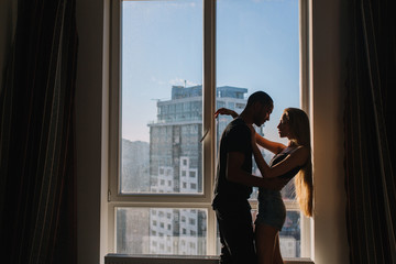 Lovely sweet moments of cute copule hugging near window in the morning in modern apartment. Being in love, hugging, relationship, home, cheerful mood, true emotions