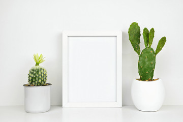 Mock up white frame with cactus plants on a shelf or desk. White shelf and wall. Portrait frame orientation.