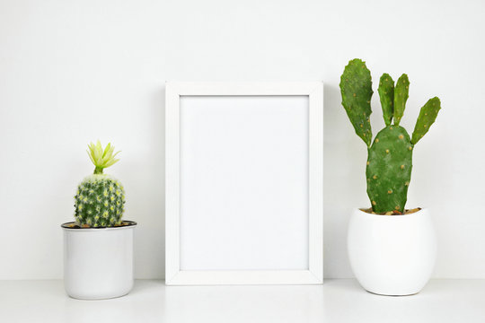 Mock up white frame with cactus plants on a shelf or desk. White shelf and wall. Portrait frame orientation.