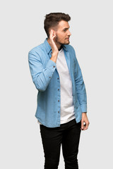 Handsome man listening to something by putting hand on the ear over grey background