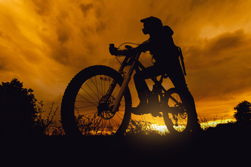Fototapeta na wymiar Downhill mountain bike rider silhouette at sunset with full face helmet