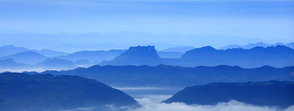 Abstract Image, Mountain Silhouettes at dawn - rolling jagged mountain peaks, cold blue color hues. Panoramic Abstract Background Image, overcast skies, layers of rolling mountains in the distance.