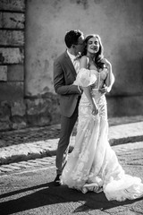 Fototapeta na wymiar Happy newlyweds. The groom hugs and kisses his beloved beautiful bride, outdoors. Black and white photo