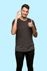 Fototapeta premium Man with black shirt showing ok sign with and giving a thumb up gesture over blue background