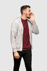 Man with sweatshirt shouting with mouth wide open to the lateral over grey background