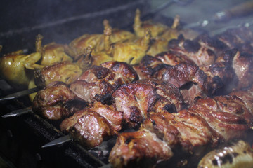 Pork and quail barbecue on skewers frying on a grill brazier