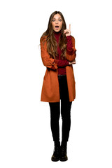 Full-length shot of Young woman with coat thinking an idea pointing the finger up on isolated white background