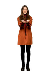 Full-length shot of Young woman with coat holding copyspace imaginary on the palm to insert an ad on isolated white background