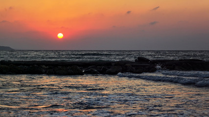 Red sun shines in evening over calm sea near beach, sky is nice sunset colour.