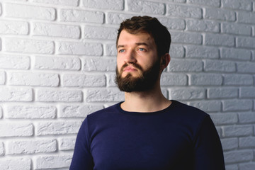 portrait of a handsome bearded man on brick wall background. Pensive hipster isolated