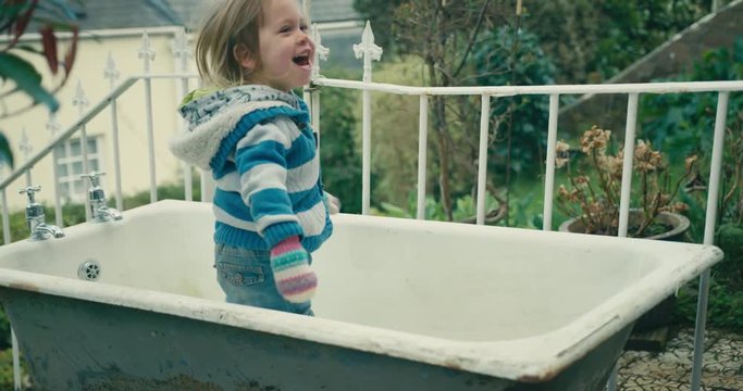 Little toddler playing peekaboo in an old bathtub outdoors in garden