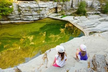 Two cute girls exploring Papingo Rock Pools, also called ovires, natural green water pools located in small smooth-walled gorge near the village of Papingo in Zagori region, Greece.
