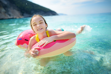 Cute young girl floating on toy ring at Myrtos beach, the most famous and beautiful beach of Kefalonia, a large coast with turqoise water and white coarse sand.