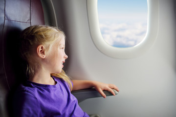 Adorable little girl traveling by an airplane. Child sitting by aircraft window and looking outside. Traveling with kids.