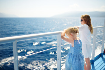 Adorable young girls enjoying ferry ride staring at the deep blue sea. Children having fun on...