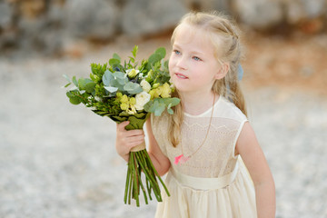 Adorable little bridesmaid holding beautiful flower bouquets after wedding cemerony outdoors.